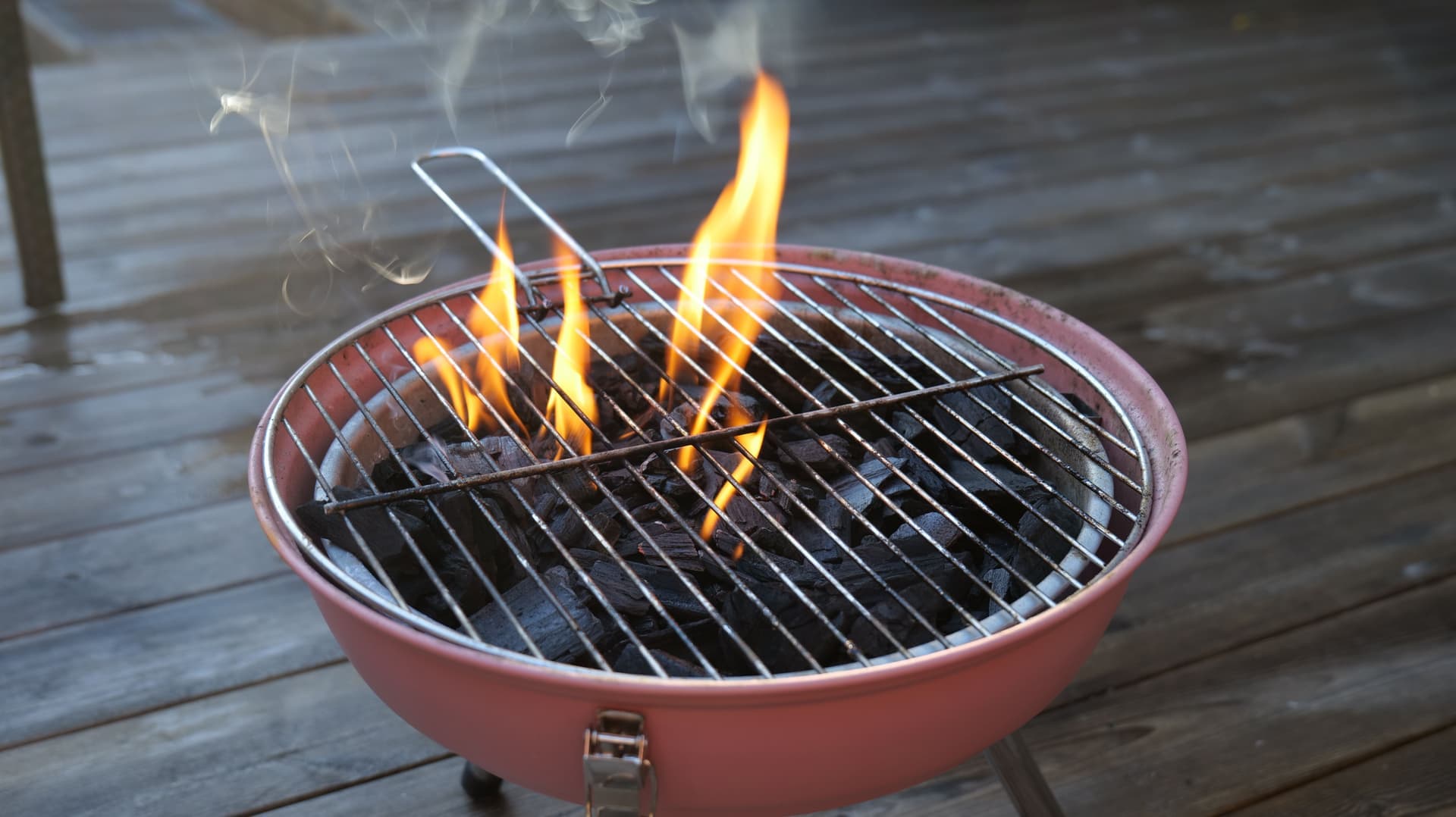 A charcoal kettle grill in a backyard with the lid off and coals lit